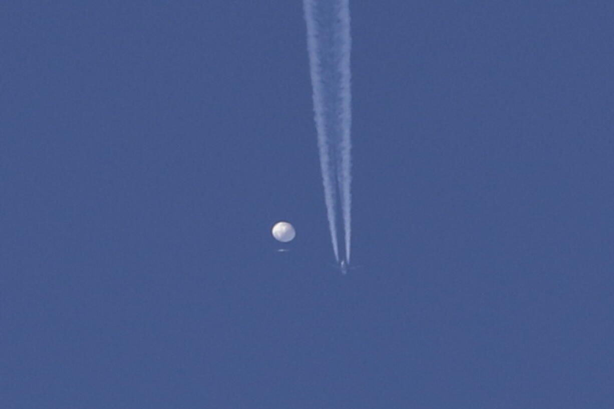 In this photo provided by Brian Branch, a large balloon drifts above the Kingstown, N.C. area, with an airplane and its contrail seen below it. The United States says it is a Chinese spy balloon moving east over America at an altitude of about 60,000 feet (18,600 meters), but China insists the balloon is just an errant civilian airship used mainly for meteorological research that went off course due to winds and has only limited "self-steering" capabilities.