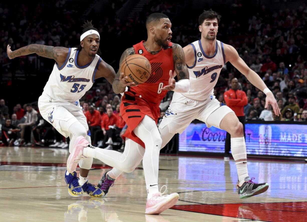 Portland Trail Blazers guard Damian Lillard, center, drives to the basket against Washington Wizards guard Delon Wright, left, and forward Deni Avdija, right, during the first half of an NBA basketball game in Portland, Ore., Tuesday, Feb. 14, 2023.