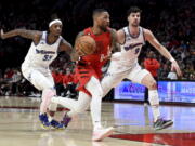 Portland Trail Blazers guard Damian Lillard, center, drives to the basket against Washington Wizards guard Delon Wright, left, and forward Deni Avdija, right, during the first half of an NBA basketball game in Portland, Ore., Tuesday, Feb. 14, 2023.