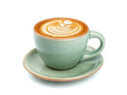 Side view of hot latte coffee with latte art in a ceramic green cup and saucer isolated on white background.