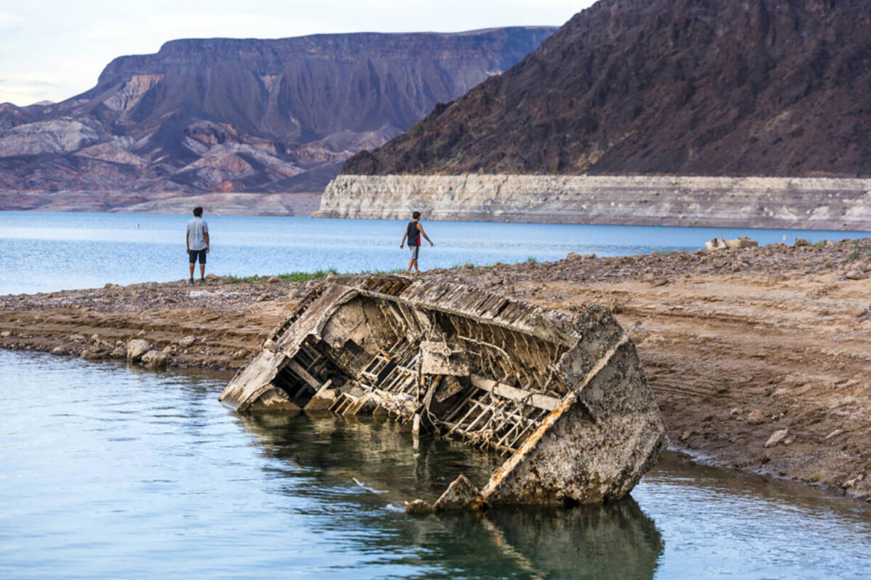 Hikers pass a previously sunken World War II-era Higgins landing craft that once was 185 feet below the surface is nearly on the shoreline as waters keep receding on July 26, 2022, near Boulder City, Nevada. (L.E.