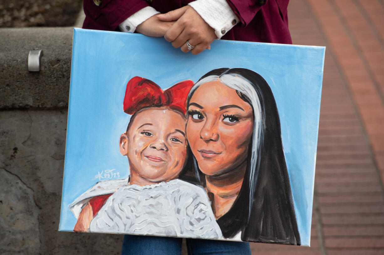 A family friend holds a painted portrait of Meshay Melendez, 27, and Layla Stewart, 7, during a community vigil for the mother and daughter Sunday in Esther Short Park's Propstra Square.
