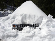 A vehicle's grill sticks out of a snow mound after a series of storms, Wednesday, March 8, 2023, in Lake Arrowhead, Calif.