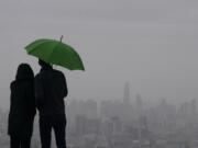 People stand under an umbrella while looking toward the skyline from Twin Peaks in San Francisco, Thursday, March 9, 2023. California is bracing for the arrival of an atmospheric river that forecasters warn will bring heavy rain, strong winds, thunderstorms and the threat of flooding even as the state is still digging out from earlier storms.