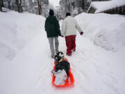 Angie Gourirand, left, and Cindy Maner, whose cars are buried in the snow, carry their groceries on a sled in Running Springs, Calif., Tuesday, Feb. 28, 2023. Beleaguered Californians got hit again Tuesday as a new winter storm moved into the already drenched and snow-plastered state, with blizzard warnings blanketing the Sierra Nevada and forecasters warning residents that any travel was dangerous. (AP Photo/Jae C.