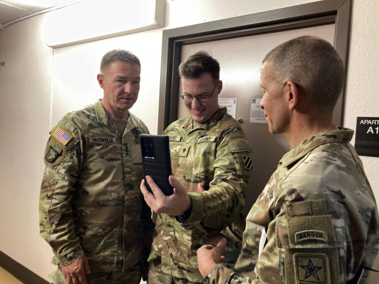 Army Chief of Staff Gen. James McConville, left, takes part in a cellphone conversation with Spc. Benjamin Soares, middle, and Sergeant Major of the Army Michael Grinston while visiting barracks in Fort Stewart, Ga., on Tuesday, March 7, 2023.