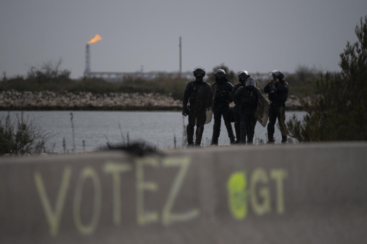 Riot police stand at the entrance of an oil depot in Fos-sur-Mer, southern France, Friday, March 24, 2023. French President Macron's office says state visit by Britain's King Charles III is postponed amid mass strikes and protests.