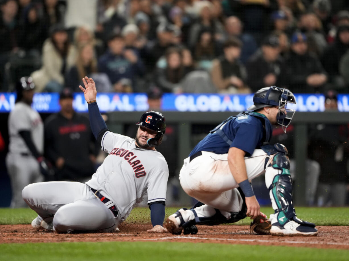 Cleveland Guardians' Mike Zunino slides home to score on a two-run single by Steven Kwan, as Seattle Mariners catcher Cal Raleigh waits for the throw during the fifth inning of a baseball game Friday, March 31, 2023, in Seattle.