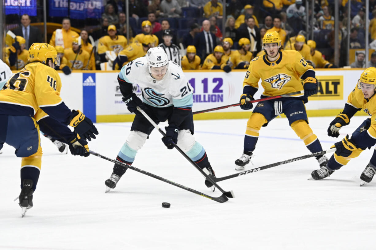 Seattle Kraken right wing Eeli Tolvanen (20) maneuvers the puck between Nashville Predators defenseman Jordan Gross (46) and center Cody Glass (8) during the first period of an NHL hockey game Thursday, March 23, 2023, in Nashville, Tenn.