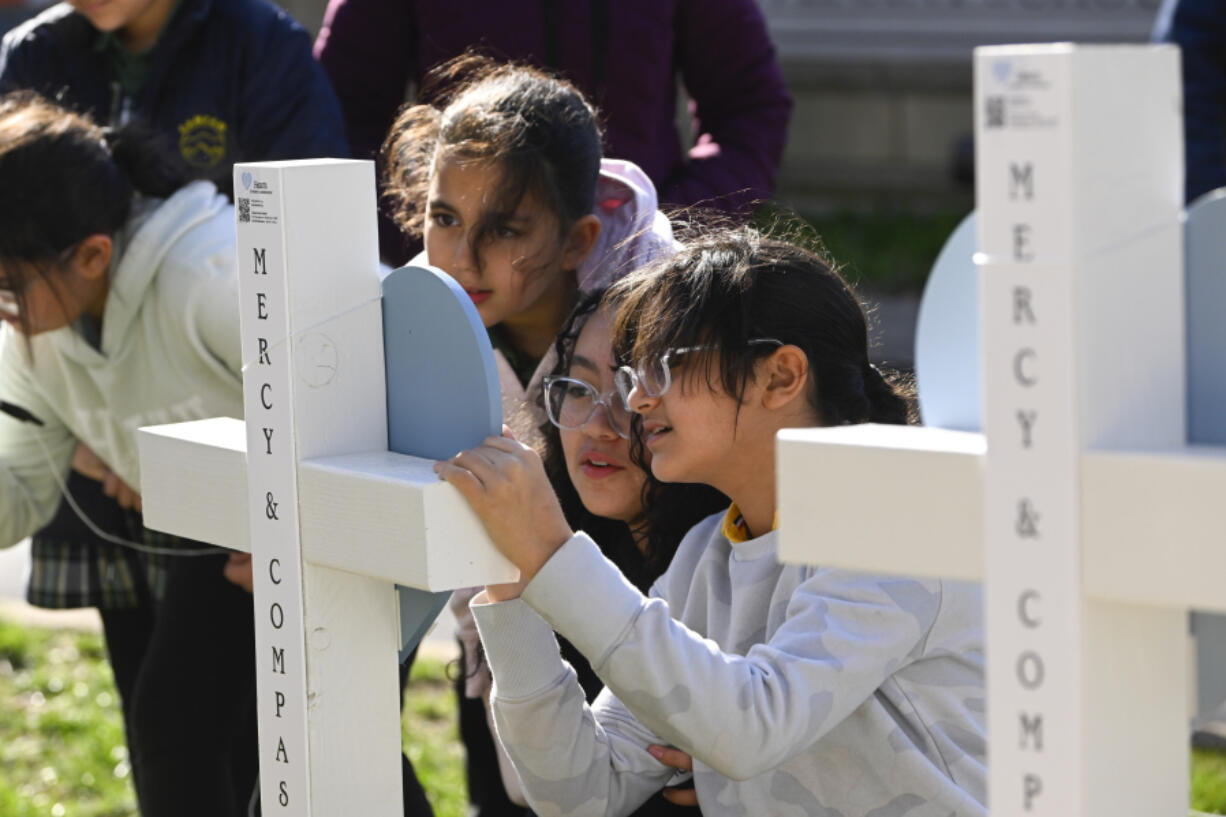 Children sign a cross at an entry to Covenant School, Tuesday, March 28, 2023, in Nashville, Tenn., which has become a memorial to the victims of Monday's deadly school shooting.