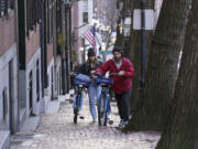 Passers-by walk their bikes up a hill in a residential area near the Statehouse on Beacon Hill, Monday, Feb. 13, 2023, in Boston. For much of the Eastern United States, the winter of 2023 has been a bust. Snow totals are far below average from Boston to Philadelphia in 2023 and warmer temperatures have often resulted in more spring-like days than blizzard-like conditions.