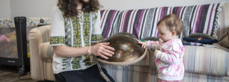 Yevhenii Hornishevskyi, left, lets his daughter Miroslava Hornishevska, 1, play with a tongue drum in their home. Hornishevskyi and his wife handmake and sell tongue drums on Etsy as their main source of income.