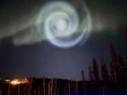 In this photo provided by Christopher Hayden, a light baby blue spiral resembling a galaxy appears amid the aurora for a few minutes in the Alaska skies near Fairbanks, Saturday, April 15, 2023.  The spiral was formed when excess fuel that had been released from a SpaceX rocket that launched from California about three hours earlier turned to ice, and then the water vapor reflected the sunlight in the upper atmosphere.