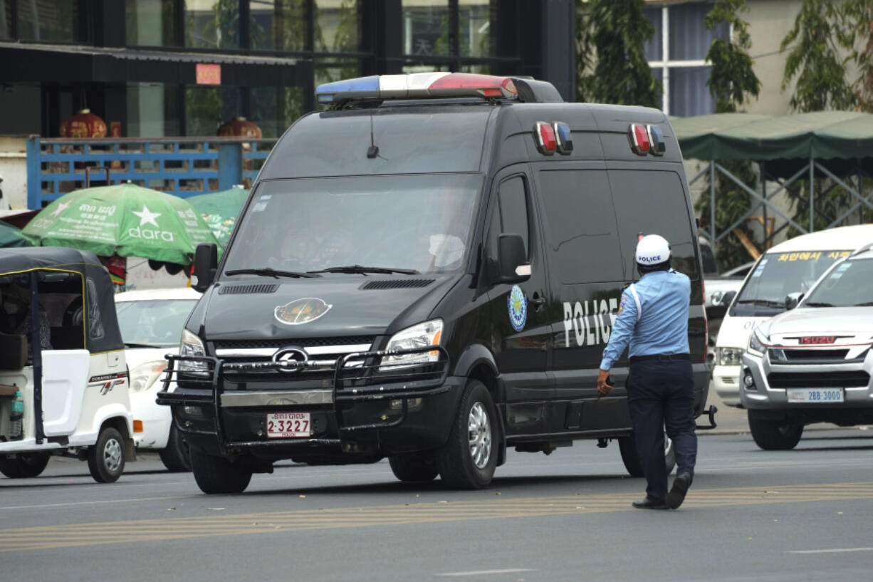 A Cambodian police man directs traffic as a convoy of police vehicles that was reportedly carrying Japanese citizens who were taken into custody on suspicion of running phone scams moves on a street on their way to Phnom Penh International Airport in Phnom Penh, Cambodia, Tuesday, April 11, 2023. Over a dozen of Japanese men detained in Cambodia in January on suspicion of taking part in phone and online scams were deported to their homeland on Tuesday, police said.