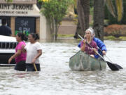 Residents paddle and walk along a flooded road Thursday, April 13, 2023, in Fort Lauderdale, Fla. Over two feet of rain fell causing widespread flooding, closing the Fort Lauderdale airport and turning thoroughfares into rivers.