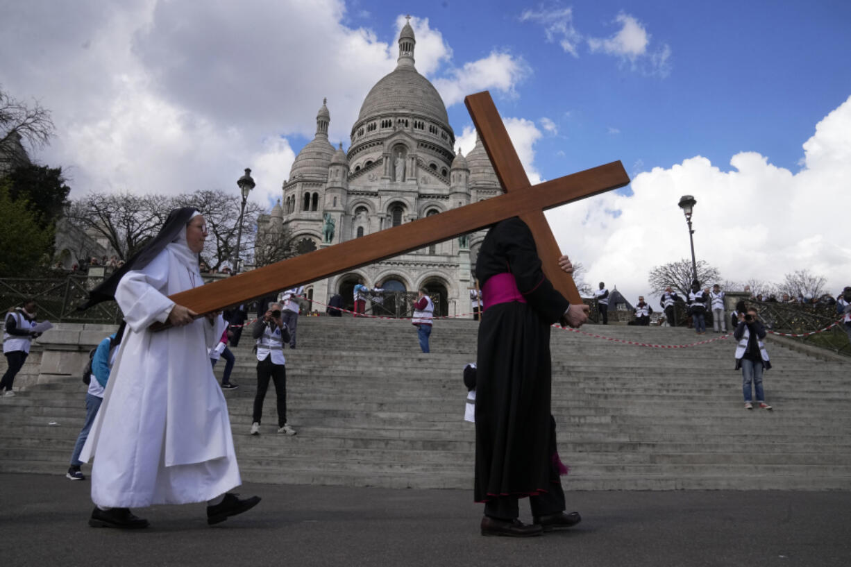 A nun helps Paris Archbishop Laurent Ulrich carrying a wooden cross in front of the Sacre-Coeur basilica, during the Way of the Cross ceremony as part of Easter celebrations, Friday, April 7, 2023 in Paris.