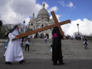 A nun helps Paris Archbishop Laurent Ulrich carrying a wooden cross in front of the Sacre-Coeur basilica, during the Way of the Cross ceremony as part of Easter celebrations, Friday, April 7, 2023 in Paris.