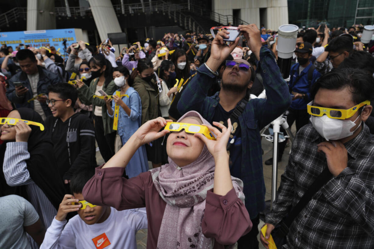 People use protective glasses to watch solar eclipse in Jakarta, Indonesia, Thursday, April 20, 2023. A rare solar eclipse will cross over remote parts of Australia, Indonesia and East Timor on Thursday.