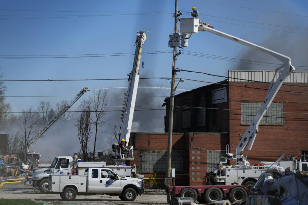 Utility workers remove utilities from the area as firefighter pour water on an industrial fire in Richmond, Ind., Wednesday, April 12, 2023. Authorities urged people to evacuate if they live near the fire. The former factory site was used to store plastics and other materials for recycling or resale.