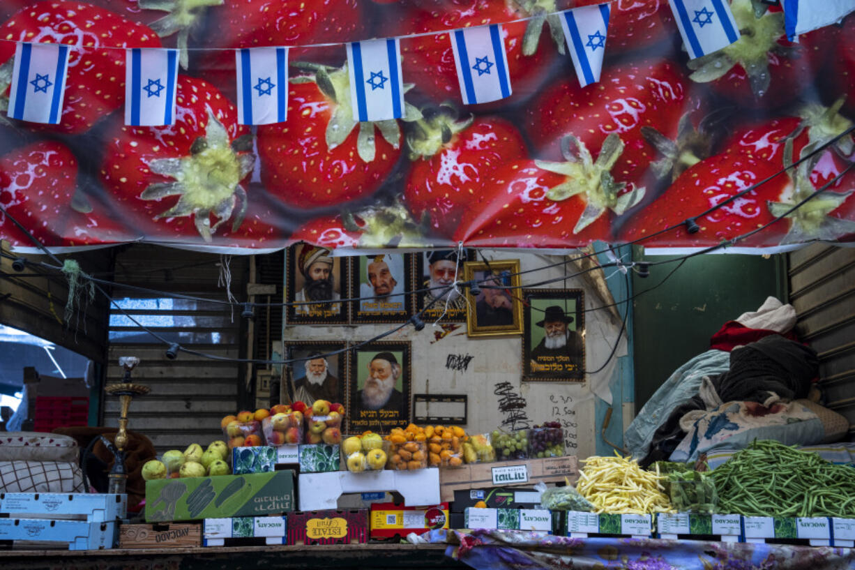 Israeli flags fly above a fruit store at a market, in Tel Aviv, Israel, Monday, April 17, 2023.