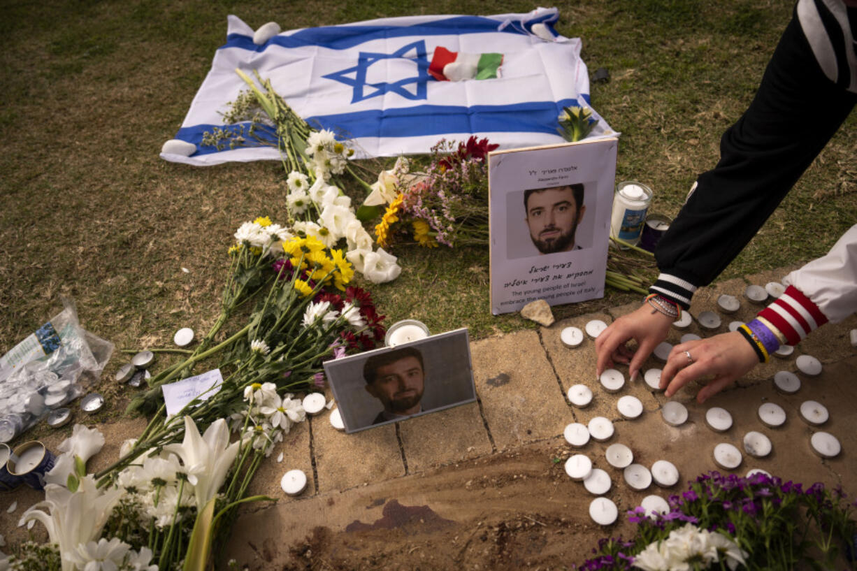 People lay flowers and candles next to photos showing Alessandro Parini, an Italian tourist who was killed in a Palestinian attack, in Tel Aviv, Israel, Saturday, April 8, 2023. Israeli authorities said an Italian tourist was killed and five other Italian and British citizens were wounded Friday when a car rammed into a group of tourists in Tel Aviv.