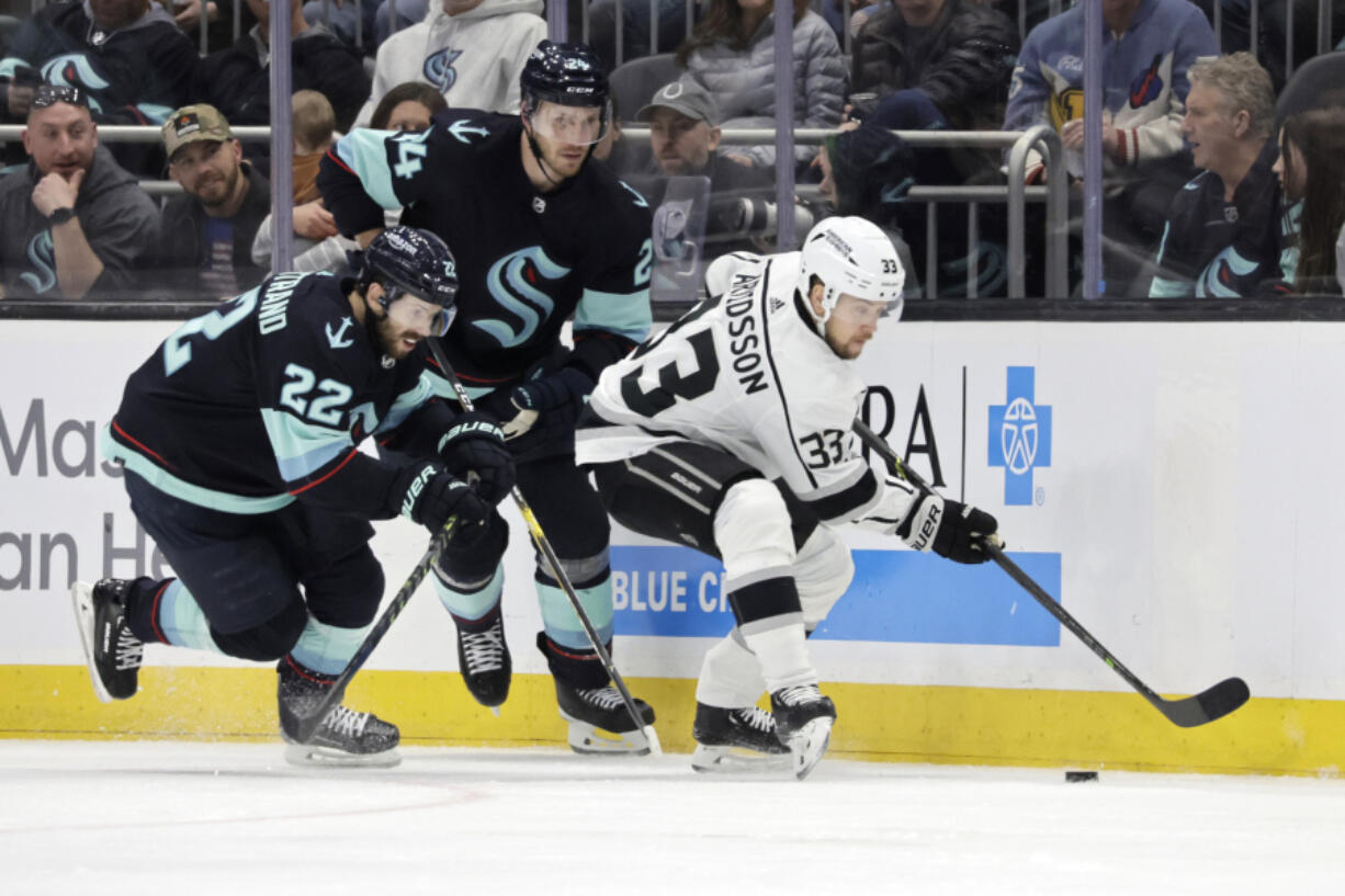 Los Angeles Kings right wing Viktor Arvidsson (33) and Seattle Kraken right wing Oliver Bjorkstrand (22) and defenseman Jamie Oleksiak (24) compete for the puck during the second period of an NHL hockey game Saturday, April 1, 2023, in Seattle.