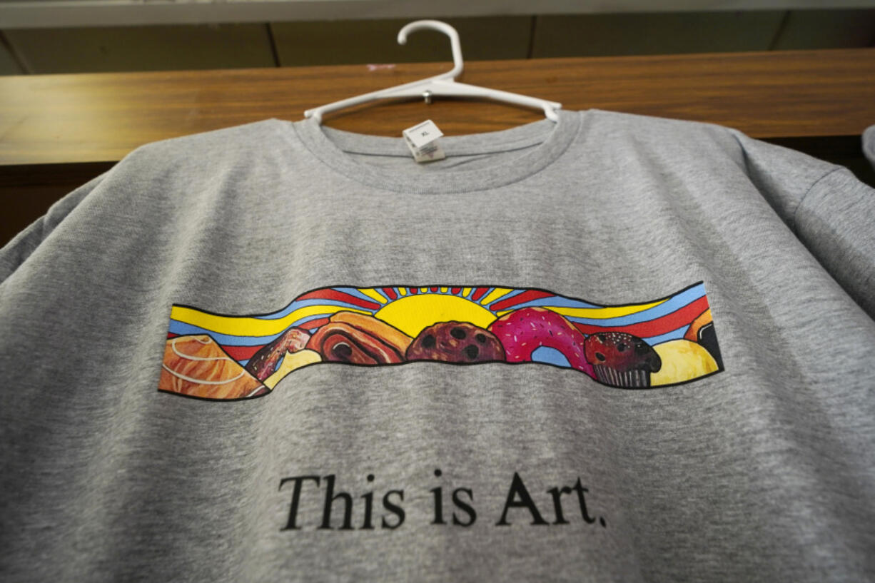 A T-shirt showing the painting displayed outside Leavitt's Country Bakery, is displayed Thursday, April 13, 2023, in Conway, N.H. Proceeds from the sale of shirts will benefit the art program at a local high school whose students painted the mural that is at the center of a zoning controversy. (AP Photo/Robert F.