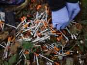 FILE - A volunteer cleans up needles used for drug injection that were found at a homeless encampment in Everett, Wash., Nov. 8, 2017. (AP Photo/Ted S.