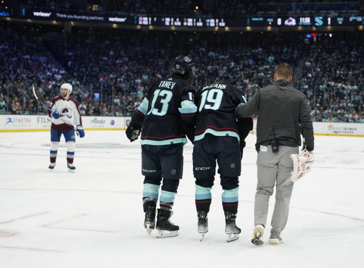 Seattle Kraken left wing Brandon Tanev (13) and a member of the Kraken staff, right, accompany left wing Jared McCann (19) off the ice after McCann was hit into the boards by Colorado Avalanche defenseman Cale Makar during the first period of Game 4 of an NHL hockey Stanley Cup first-round playoff series Monday, April 24, 2023, in Seattle.