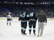 Seattle Kraken left wing Brandon Tanev (13) and a member of the Kraken staff, right, accompany left wing Jared McCann (19) off the ice after McCann was hit into the boards by Colorado Avalanche defenseman Cale Makar during the first period of Game 4 of an NHL hockey Stanley Cup first-round playoff series Monday, April 24, 2023, in Seattle.