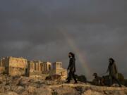 Women wearing face masks walk with their dogs March 31, 2021, at the Areopagus hill, in front of the ancient Acropolis hill, as a rainbow is seen in the Athenian sky.