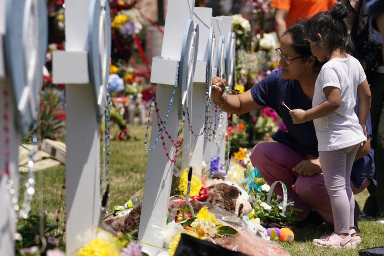 A woman signs a cross as a child looks on at a makeshift memorial by the mall where several people were killed in Saturday's mass shooting, Monday, May 8, 2023, in Allen, Texas.