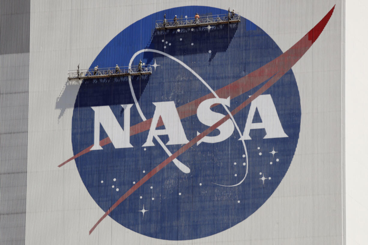 FILE - Workers on scaffolding repaint the NASA logo near the top of the Vehicle Assembly Building at the Kennedy Space Center in Cape Canaveral, Fla., May 20, 2020.