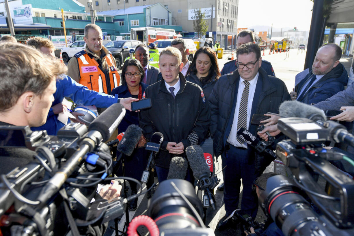 New Zealand Prime Minister Chris Hipkins, center, speaks to media near the site of a fatal hostel fire in Wellington, New Zealand, Tuesday, May 16, 2023. Several people were killed after a fire broke out overnight at the four-story building.