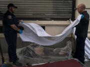 FILE - Forensic assistant Laurentiu Bigu, left, and investigator Ryan Parraz from the Los Angeles County coroner's office cover the body of a homeless man found dead on a sidewalk in Los Angeles on April 18, 2022. The 60-year-old man died from the effects of methamphetamine, according to his autopsy report. Drug overdose deaths in the U.S. went up slightly in 2022 after two big leaps during the pandemic. (AP Photo/Jae C.