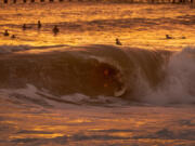 With the golden glow of the sunset, surfer Dylan Sloan, 15, of Huntington Beach, gets a coveted tube ride while surfing big waves generated by winter storms at the Seal Beach pier in January. (Allen J.