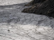 A couple hold their hands while walking on the melting Tsanfleuron Glacier above Les Diablerets on Aug. 6, 2022. Following several heatwaves blamed by scientists on climate change, Switzerland is seeing its alpine glaciers melting at an increasingly rapid rate.