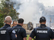 Vancouver Police officers talk while a house fire smolders Thursday, June 8, 2023, on Lower River Road west of Vancouver. Two people were transported to the hospital as a result of the fire.