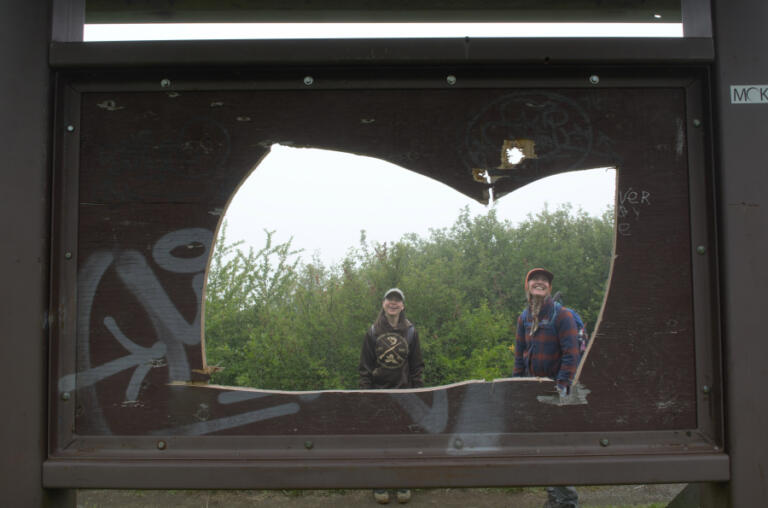 Heather Evans, left, and Katie Rinker look at a vandalized signpost at Ed's Trail Trailhead while waiting for other crew members.