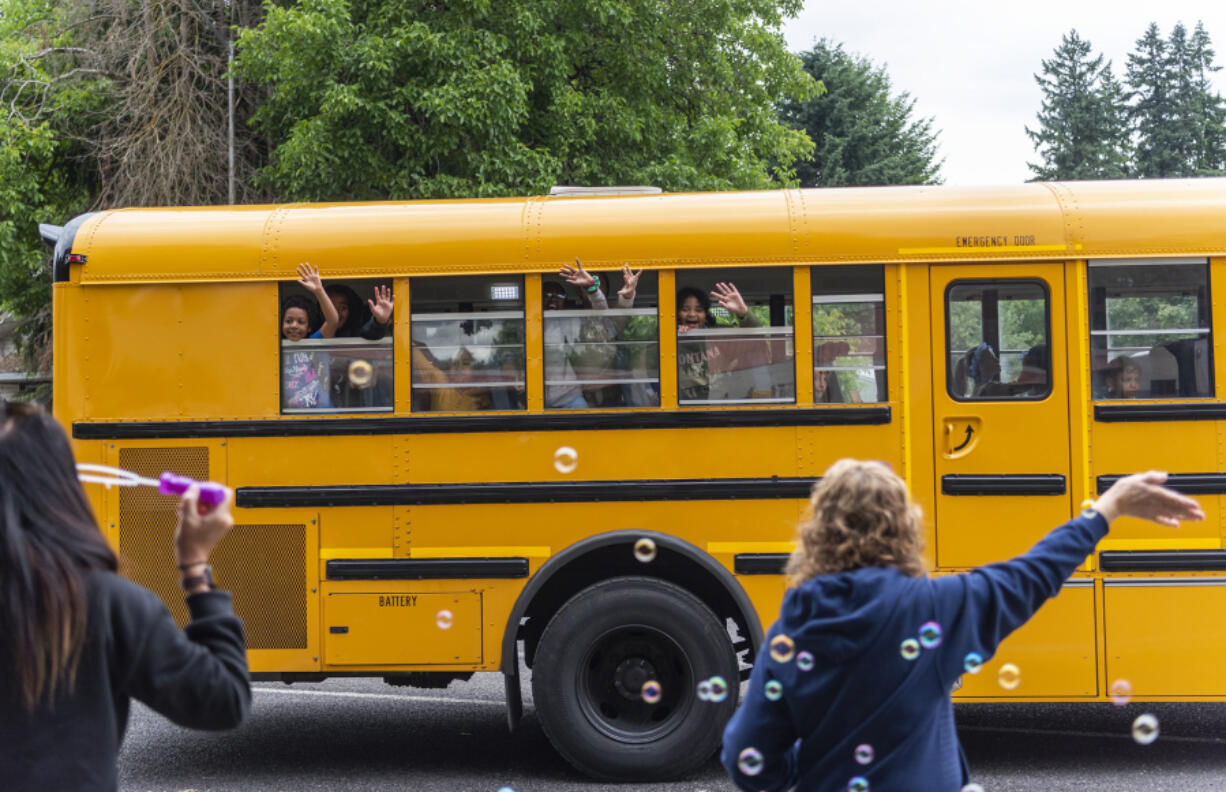 Students wave goodbye to faculty and staff as their bus drives away Tuesday following the last day of school at Eleanor Roosevelt Elementary School.
