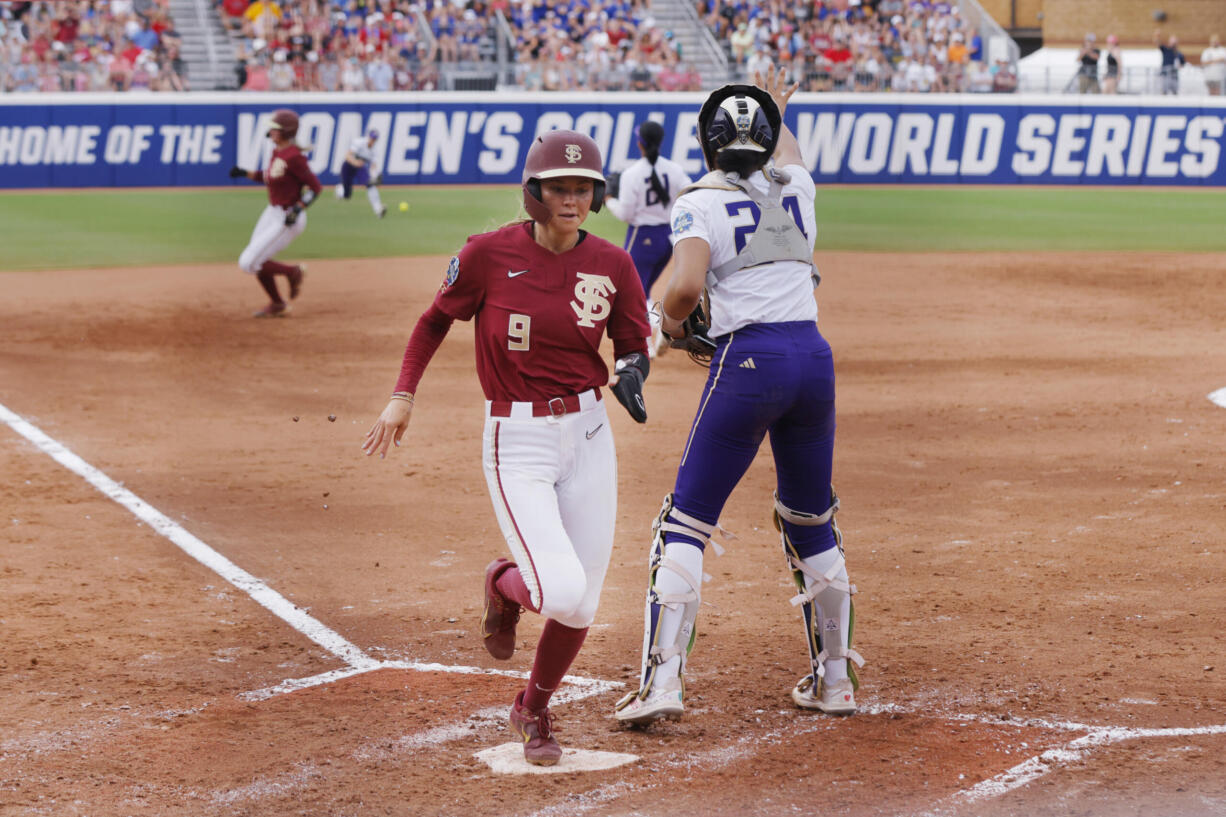 Florida State's Devyn Flaherty (9) scores next to Washington catcher Sydney Stewart during the second inning of an NCAA softball Women's College World Series game Saturday, June 3, 2023, in Oklahoma City.