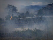 A firefighter directs water on a grass fire on an acreage behind a residential property in Kamloops, British Columbia, Monday, June 5, 2023. No structures were damaged but firefighters had to deal with extremely windy conditions while putting out the blaze.