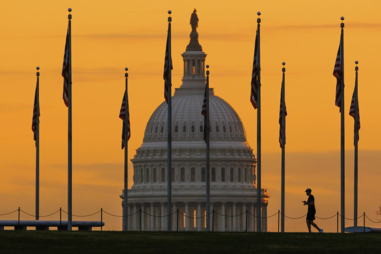 FILE - An early morning pedestrian is silhouetted against sunrise as he walks through the American flags on the National Mall with the U..S Capitol Building in the background in Washington Nov. 7, 2022. Americans on the right and left have a lot more in common than they might think -- including their strong distrust of each other. The results of the survey, conducted by NORC at the University of Chicago and the nonprofit group Starts With Us, reveal a stark truth at the source of the polarization that has a powerful grip on American politics: While most Americans agree on the core principals underlying American democracy, they no longer recognize that the other side holds those values too.(AP Photo/J.