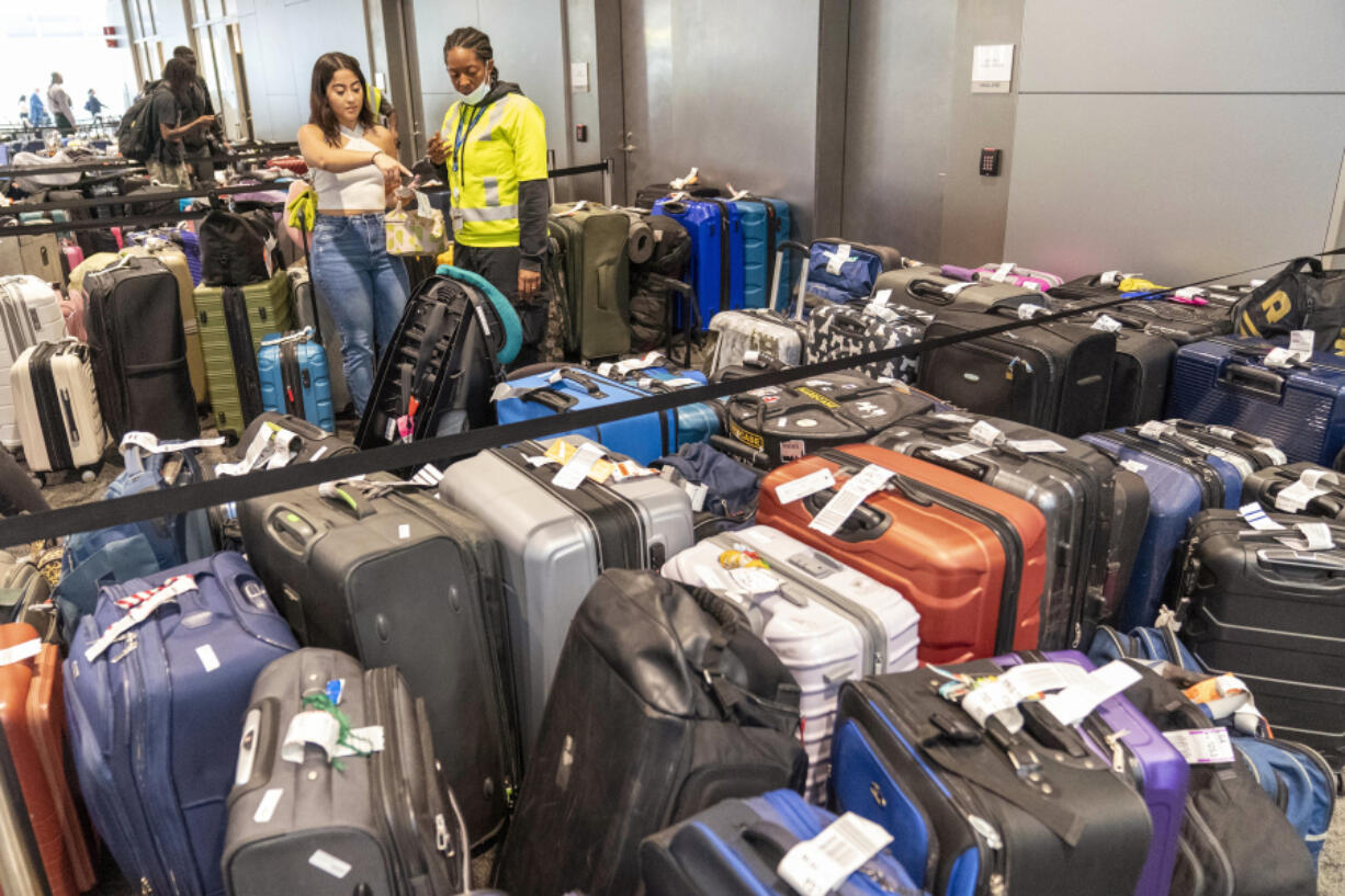 An airline employee, right, helps a traveler find her suitcase amongst the unclaimed luggage in the arrivals area of Terminal B at LaGuardia Airport, Tuesday, June 27, 2023, in New York.  Travelers waited out widespread delays at U.S. airports on Tuesday, an ominous sign heading into the long July 4 holiday weekend, which is shaping up as the biggest test yet for airlines that are struggling to keep up with surging numbers of passengers.