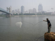 FILE - A man tosses a fishing net into the Ohio River as smoke from wildfires is visible over downtown Cincinnati, June 28, 2023. Forecasters say there won't be large breaks for much of America anytime soon from eye-watering dangerous smoke from fire-struck Canada. (AP Photo/Joshua A.