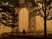 FILE - A man talks on his phone as he looks through the haze at the George Washington Bridge in Fort Lee, N.J., June 7, 2023. Thick, smoky air from Canadian wildfires made for days of misery in New York City and across the U.S. Northeast this week. But for much of the rest of the world, breathing dangerously polluted air is an inescapable fact of life -- and death.