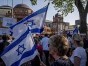 Women hold Israeli flags as they take part in a demonstration against a concert later the day of former Pink Floyd musician Roger Waters in the Festhalle, background, in Frankfurt, Germany, Sunday, May 28, 2023. The Festhalle was the the place where in the night of broken glasses 1938 about 3000 Jewish men where gathered to deport them to concentration camps.