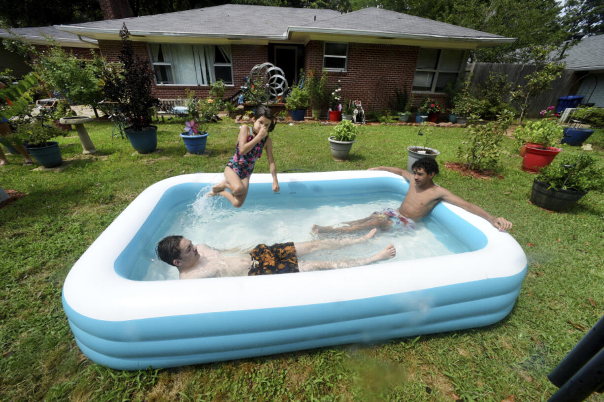 From left to right, Cason Bullis, Mya Kampfer and Caleb Dessos find a way to cool off with their inflatable pool, Saturday afternoon, June 17, 2023, in the front yard of their Shreveport, La., house that continues to be without electricity because of a storm on Friday evening, June 16.