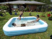 From left to right, Cason Bullis, Mya Kampfer and Caleb Dessos find a way to cool off with their inflatable pool, Saturday afternoon, June 17, 2023, in the front yard of their Shreveport, La., house that continues to be without electricity because of a storm on Friday evening, June 16.