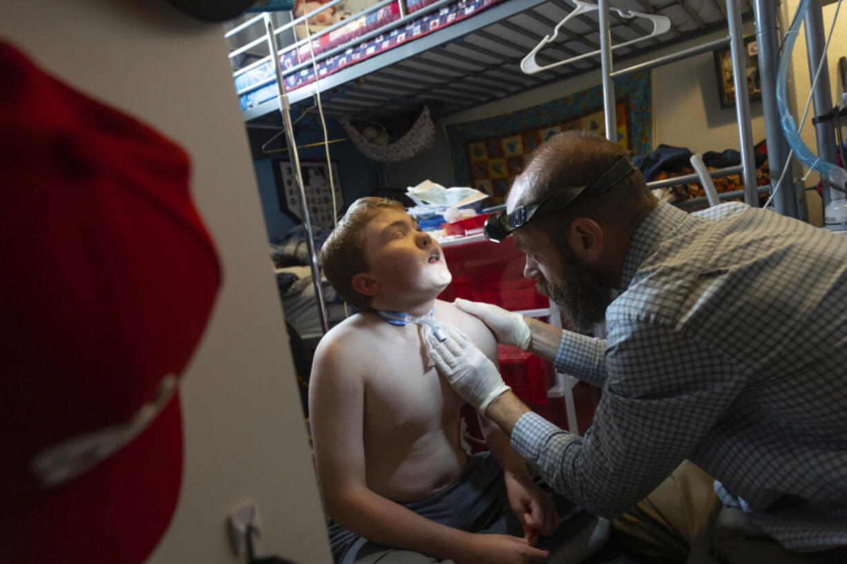 Nathan Hill changes the trach tube on his son Brady at their home in Meridian, Idaho, June 19, 2023. Brady survived a rare brain cancer as a baby, but requires round the clock care. Each morning Nate and his wife spend about 3 hours with Brady performing his medical cares and getting him ready for the day. Families of severely disabled children across the country are worried about the future of crucial Medicaid payments they started receiving to provide care during the COVID-19 pandemic.